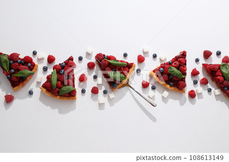 Pieces of berry pie, raspberries, blueberries and sugar on white background, top view 108613149
