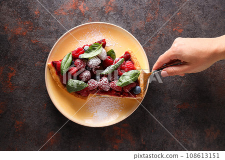 Pieces of berry pie on plate, female hand on dark gray background, top view Pieces of berry pie on plate, female hand on dark gray background, top view 108613151