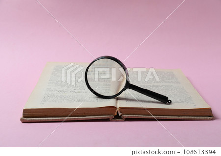 Magnifying glass on open book on pink background 108613394