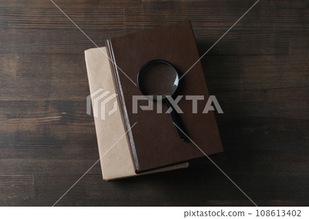 Magnifying glass on books on wooden background, top view 108613402