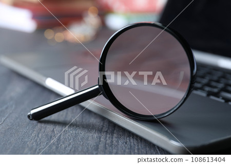 Magnifying glass on laptop keyboard on wooden background, close up 108613404