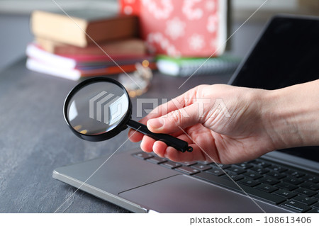 Magnifying glass in hand and laptop on wooden background 108613406