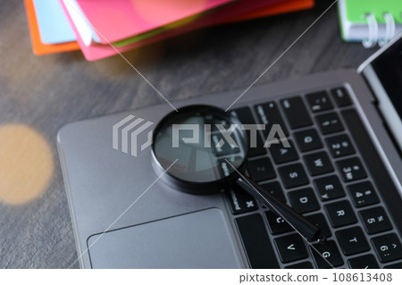 Magnifying glass on laptop keyboard on wooden background Magnifying glass on laptop keyboard on wooden background 108613408