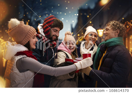 Group portrait of adorable smiling people in cozy fair atmosphere standing outdoor and having fun while drinking hot warming drink. Group portrait of adorable smiling people in cozy fair atmosphere standing outdoor and having fun while drinking hot warming drink. 108614370