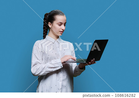 Serious teenage high school student girl using laptop on blue background Serious teenage high school student girl using laptop on blue background 108616282