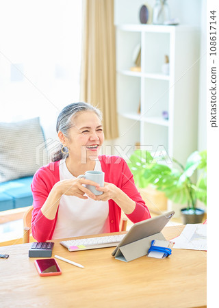 Senior woman taking a break with a mug while working from home 108617144