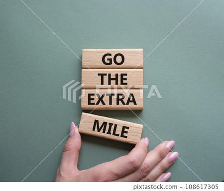 Go the extra mile symbol. Wooden blocks with words Go the extra mile. Businessman hand. Beautiful grey green background. Business and Go the extra mile concept. Copy space. 108617305