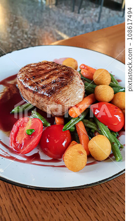 Beef steak with salad. Potato balls and various vegetables on a colored plate. Beef steak with salad. Potato balls and various vegetables on a colored plate. 108617494
