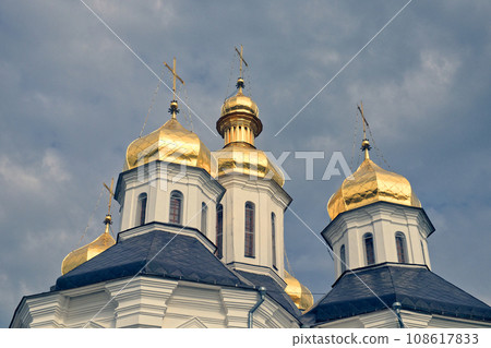 The golden domes of a Orthodox Church, standing majestically against a backdrop of a clear blue sky. Gilded domes of an ancient Orthodox church against the sky. 108617833
