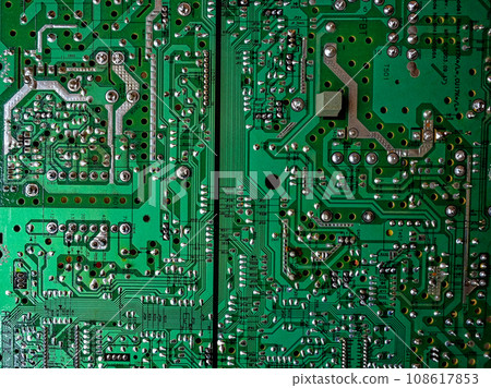 A close-up reveals the intricacies of a green computer circuit board, with various silver and gold components adorning its surface, resembling a technological landscape. 108617853