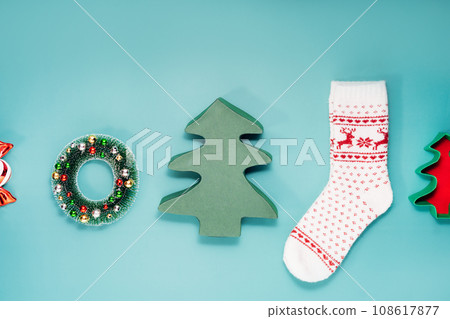 Minimalist Christmas mood concept. Turquoise Background with Christmas attributes as Christmas tree shape gift boxes, warm socks with deer pattern, decorative wreath. Flat lay, top view. Copy space. Minimalist Christmas mood concept. Turquoise Background with Christmas attributes as Christmas tree shape gift boxes, warm socks with deer pattern, decorative wreath. Flat lay, top view. Copy space. 108617877