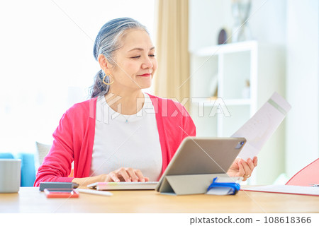 Senior woman operating a computer in her room Senior woman operating a computer in her room 108618366