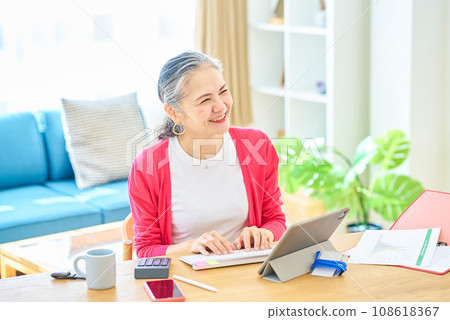 Senior woman operating a computer in her room Senior woman operating a computer in her room 108618367