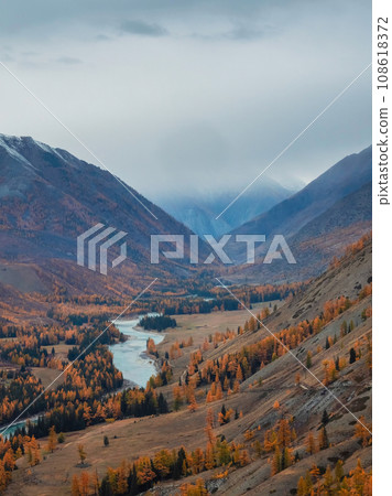 Colorful autumn landscape with golden leaves on trees along wide turquoise mountain river in misty morning. Awesome vertical alpine scenery with big mountain river in gold autumn colors in fall time. Colorful autumn landscape with golden leaves on trees along wide turquoise mountain river in misty morning. Awesome vertical alpine scenery with big mountain river in gold autumn colors in fall time. 108618372