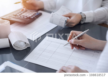 Two accountants use a calculator and tablet computer for counting taxes or revenue balance. Business, audit, and taxes concepts 108618517