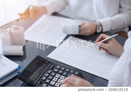 Two accountants use a calculator and laptop computer for counting taxes or revenue balance. Business, audit, and taxes concepts 108618518