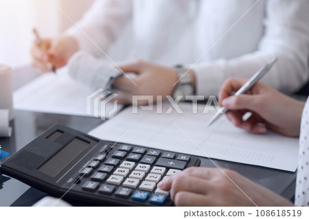 Two accountants use a calculator and laptop computer for counting taxes or revenue balance. Business, audit, and taxes concepts 108618519