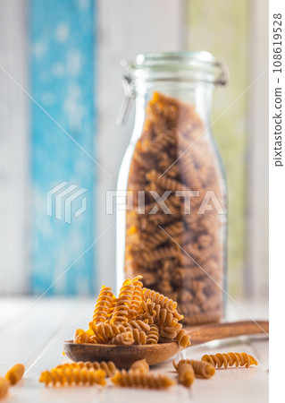 Raw whole grain fusilli pasta. Uncooked pasta on wooden spoon. Raw whole grain fusilli pasta. Uncooked pasta on wooden spoon. 108619528