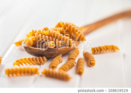Raw whole grain fusilli pasta. Uncooked pasta on wooden spoon. Raw whole grain fusilli pasta. Uncooked pasta on wooden spoon. 108619529