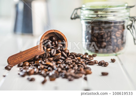 Roasted coffee beans in wooden scoop on white kitchen table. Roasted coffee beans in wooden scoop on white kitchen table. 108619533