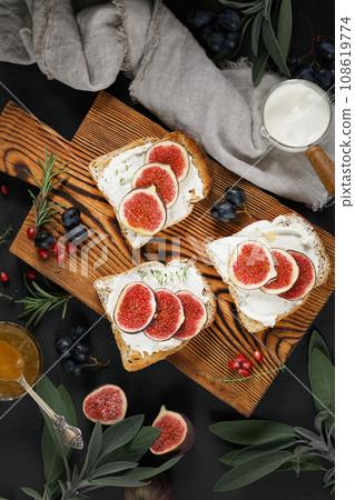 Sandwiches with ricotta, fresh figs and honey on rustic wooden board over black backdrop, vertical top view Sandwiches with ricotta, fresh figs and honey on rustic wooden board over black backdrop, vertical top view 108619774