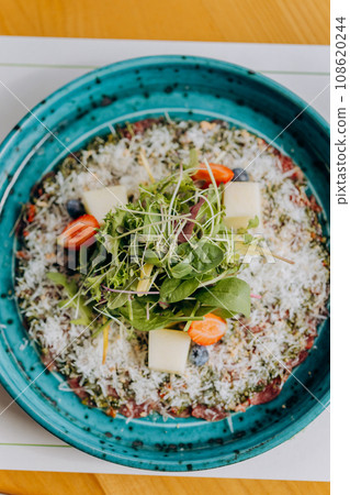 Beef carpaccio with pesto sauce and parmigiano cheese decorated by salad and fruit. Restaurant menu 108620244