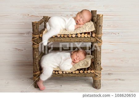 Tiny newborn twin boys in white bodysuits against a light wood background. Newborn twins sleep on a bunk wooden bed. The boys. Professional studio photography. 108620650