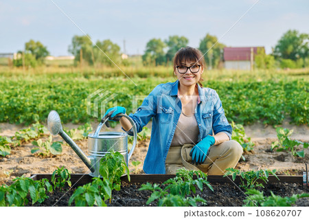 Woman with watering can, smiling female looking at camera at vegetable garden Woman with watering can, smiling female looking at camera at vegetable garden 108620707
