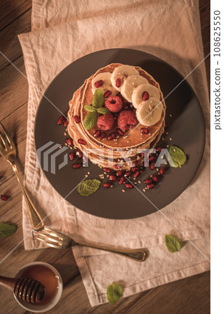 Pancakes with raspberries, banana slices, pomegranate seeds and honey 108625550