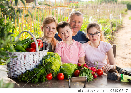 Smiling family sitting outdoors at table with harvested vegetables 108626847