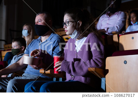 father and his daughter in masks sitting at premiere in cinema father and his daughter in masks sitting at premiere in cinema 108627017