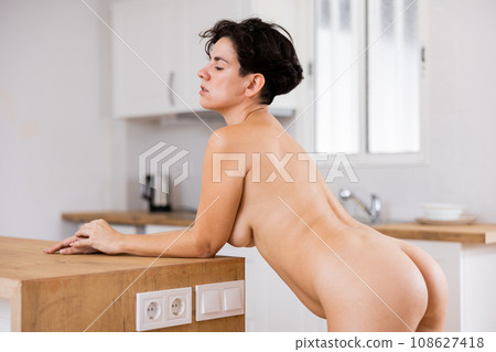 Naked woman standing near countertop at kitchen Naked woman standing near countertop at kitchen 108627418