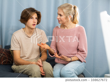 Frowning teenager listening to reprimanding from his mother at home 108627672