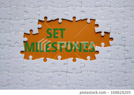 Set milestones symbol. Concept word Set milestones on white puzzle. Beautiful orange background. Business and Set milestones concept. Copy space Set milestones symbol. Concept word Set milestones on white puzzle. Beautiful orange background. Business and Set milestones concept. Copy space 108628205