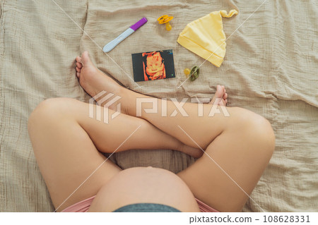 A composition of essential pregnancy attributes: a positive pregnancy test, ultrasound image, tiny pacifier, and a soft baby's cap, embodying the journey to motherhood 108628331