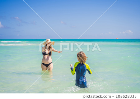 A radiant pregnant mother and her excited son share a tender moment on a serene, snow-white beach, celebrating family love amidst nature's beauty A radiant pregnant mother and her excited son share a tender moment on a serene, snow-white beach, celebrating family love amidst nature's beauty 108628333