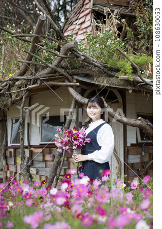 In front of a small hut, cosmos garden, woman holding a bouquet of flowers In front of a small hut, cosmos garden, woman holding a bouquet of flowers 108630053