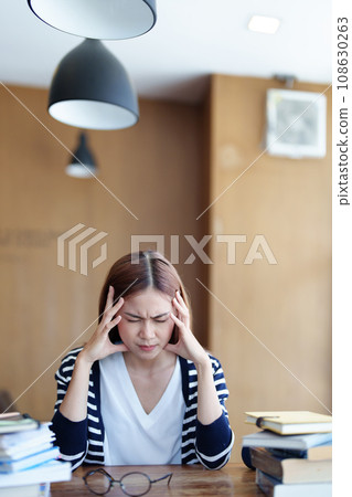 A portrait of an Asian teenage girl showing headaches and discouragement from studying in the library. 108630263