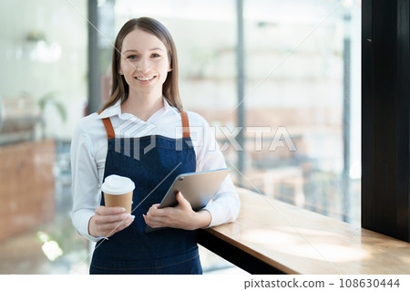 Starting and opening a small business, a young Asian woman showing a smiling face in an apron standing in front of a coffee shop bar counter. Business Owner, Restaurant, Barista, Cafe, Online SME. Starting and opening a small business, a young Asian woman showing a smiling face in an apron standing in front of a coffee shop bar counter. Business Owner, Restaurant, Barista, Cafe, Online SME. 108630444