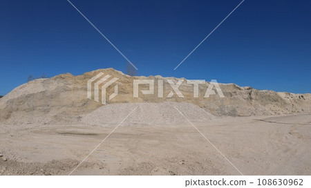 piles of white stone and sand at a mining site, on a sunny day, against a blue sky, limestone quarry with hills of extracted rock, industrial lime mining outdoors piles of white stone and sand at a mining site, on a sunny day, against a blue sky, limestone quarry with hills of extracted rock, industrial lime mining outdoors 108630962