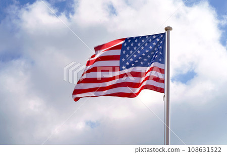 Large American flag waving on flag pole with cloud blue sky. Windy and sunny day with waving stars and striped flag Large American flag waving on flag pole with cloud blue sky. Windy and sunny day with waving stars and striped flag 108631522
