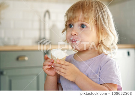 Baby girl enjoying ice cream. Pretty little toddler eating an ice-cream indoors, at home. Dining room background. Small child eats plombir and cream messy on her mouth. Cute kid with tasty sweet food. Baby girl enjoying ice cream. Pretty little toddler eating an ice-cream indoors, at home. Dining room background. Small child eats plombir and cream messy on her mouth. Cute kid with tasty sweet food. 108632508