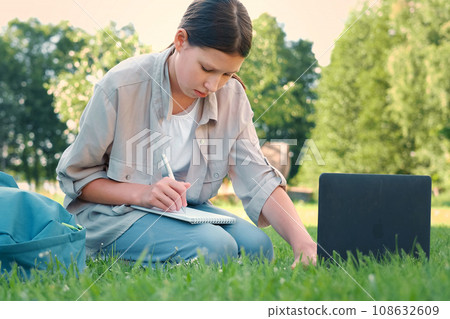 Teenage schoolgirl studying reading her books, tablet and notebook, sitting outdoors. Back to school. Student girl lying on the green grass using laptop in the college yard or park. Distance learning. Teenage schoolgirl studying reading her books, tablet and notebook, sitting outdoors. Back to school. Student girl lying on the green grass using laptop in the college yard or park. Distance learning. 108632609