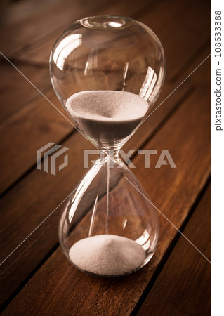 Hourglass containing white sand on a rustic wooden board 108633388