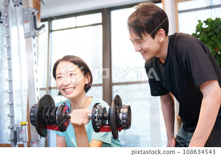 A woman and trainer (dumbbells) exercising at a sports gym 108634543