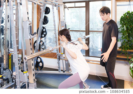 Woman and trainer exercising at the gym (barbell squat) 108634585