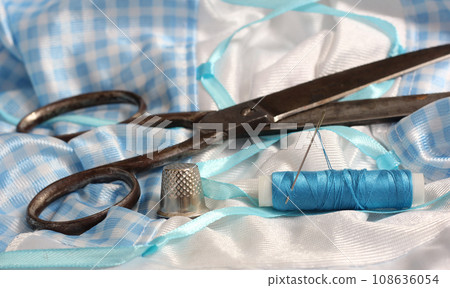 Spool of Blue Thread, Thimble and Needle on Blue and White Fabric 108636054