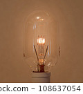 An oblong incandescent light bulb with a filament that glows slightly and gently. 108637054
