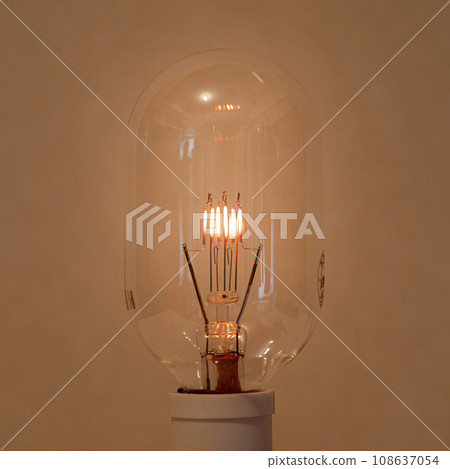 An oblong incandescent light bulb with a filament that glows slightly and gently. 108637054