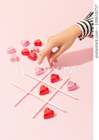 Female hand playing tic tac toe game with heart shaped candies on pink background Female hand playing tic tac toe game with heart shaped candies on pink background 108639757
